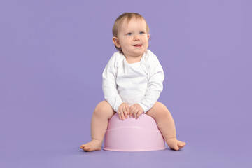 Little child sitting on baby potty against violet background