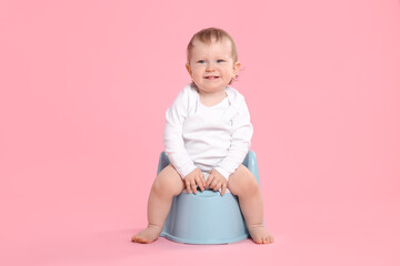 Little child sitting on baby potty against pink background