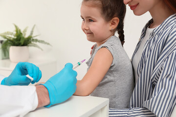 Children's hepatitis vaccination. Mother with her daughter in clinic. Doctor giving injection to...