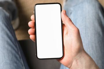 Man holding smartphone with blank screen indoors, top view. Mockup for design