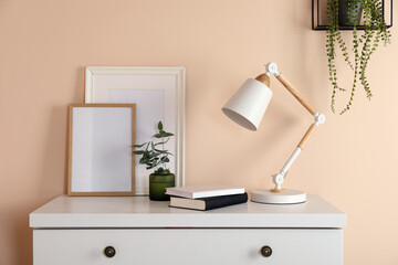 Stylish modern desk lamp, books and plant on white chest of drawers near beige wall indoors