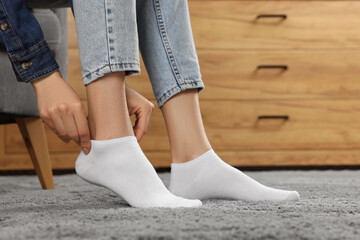 Woman putting on white socks at home, closeup