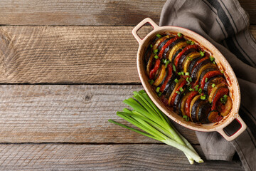Delicious ratatouille and green onions on wooden table, flat lay. Space for text