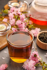 Traditional ceremony. Cup of brewed tea, teapot and sakura flowers on grey table, closeup
