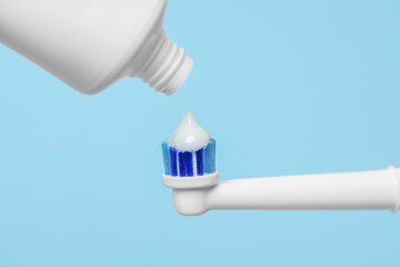 Fototapeta na wymiar Electric toothbrush with paste on light blue background, closeup