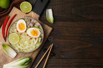 Obraz na płótnie Canvas Bowl of delicious rice noodle soup with meat and egg on wooden table, flat lay. Space for text