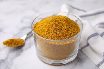 Glass with curry powder on white marble table, closeup