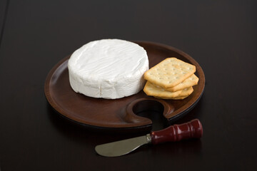 Brie and butter cracker on a wooden cheese plate with cheese knife