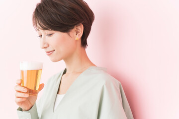 ビールを美味しそうに飲む日本人女性/ピンク背景