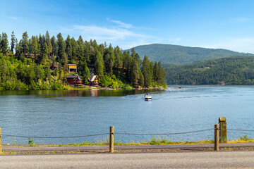A motorboat with American flag on the lake with waterfront homes and docks behind at Lake Coeur...