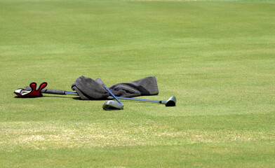 Obraz premium Wet towel and two golf clubs lying on the green grass at the golf course. Sunny day.