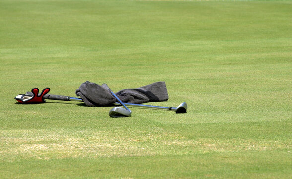 Wet towel and two golf clubs lying on the green grass at the golf course. Sunny day.