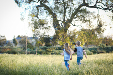 Boy and girl running through long grass playing soccer at the park. Aussie kids having fun outdoors...