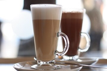 Cafe Latte in a glass with hot chocolate in background