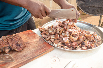 Hand of an african man or chef holding kitchen knife and cutting barbequed meat into small pieces...
