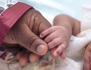 Hand of a caring African Nigerian woman or mother tenderly holding the little fingers of her new...
