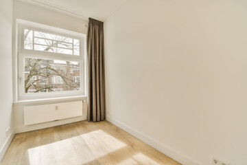 an empty room with wood floors and white walls, there is a large window in the wall has brown curtains