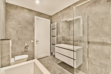 a modern bathroom with white fixtures and grey tiles on the walls, along with a freestanding bathtub next to the sink