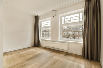 an empty room with wood flooring and two large windows in the photo is taken from inside, looking out to outside
