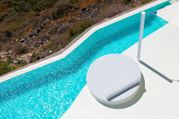 Santorini island, Greece. Luxury swimming pool with blue water and white chaise lounge.