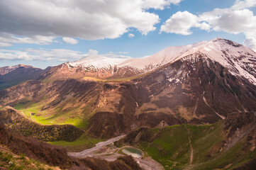 Beautiful mountain landscape, clouds over the peaks of the mountains, sunny day and green grass on mountain peaks next to the remnants of snow