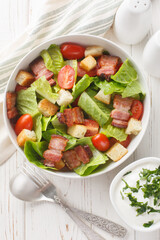 BLT salad is loaded with fresh lettuce, crispy bacon, bright tomatoes croutons closeup on the plate on the table. Vertical top view from above