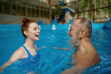 Happy smiling mature man and young woman swimming in pool