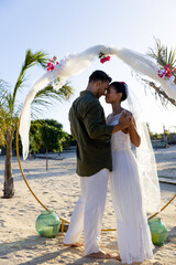 Side view of caucasian newlywed couple holding hands and standing at beach at wedding ceremony
