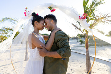 Side view of newlywed caucasian couple with face to face standing at beach at wedding ceremony