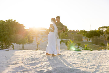 Newlywed caucasian couple dancing on sandy beach against clear sky at sunset, copy space