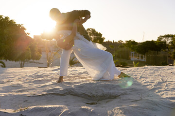 Caucasian newlywed couple dancing on sandy beach against clear sky at sunset, copy space