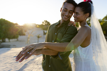 Smiling newlywed caucasian couple showing wedding rings while standing at beach against clear sky