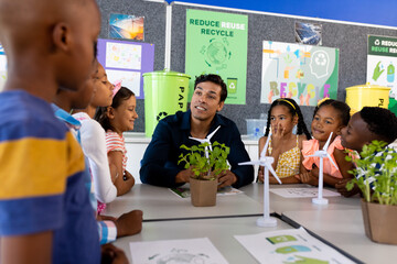 Happy diverse male teacher and children in elementary school class with windmills and plants