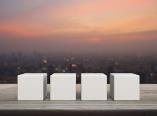 Four white block cubes on wooden table over blur of cityscape on warm light sundown