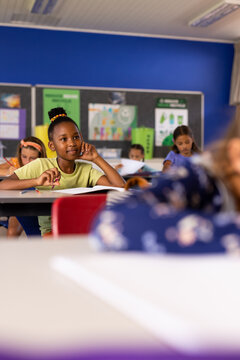 Happy diverse schoolgirls listening at desks in elementary school class