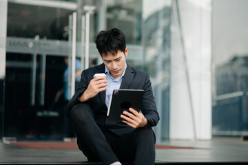 Young Asian business man working at outside business center with laptop, tablet, smartphone and taking notes on the paper.