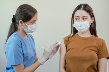 Female doctor wearing mask holding syringe giving vaccinations to patient for protection. During...