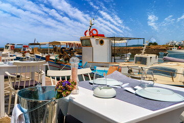 Tables and chairs of restaurant by waterfront with fishing boats in
