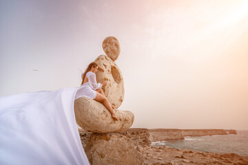 Woman sky stone. Lady stands on stone sculpture with ocean view. She is dressed in a white long...