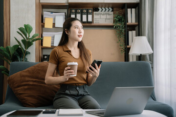 woman sits in a office working on smartphone, laptop and enjoys a coffee.