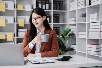 businesswoman sits in a office working on laptop, smartphone and enjoys a coffee.