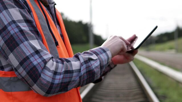 A railway traffic engineer inspector at a freight station takes notes on his tablet computer.	

