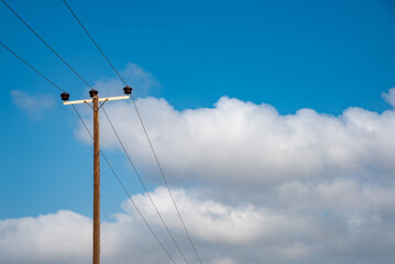 Electricity transmission lines transferring electrical energy outdoors. Blue cloudy sky. Copy space
