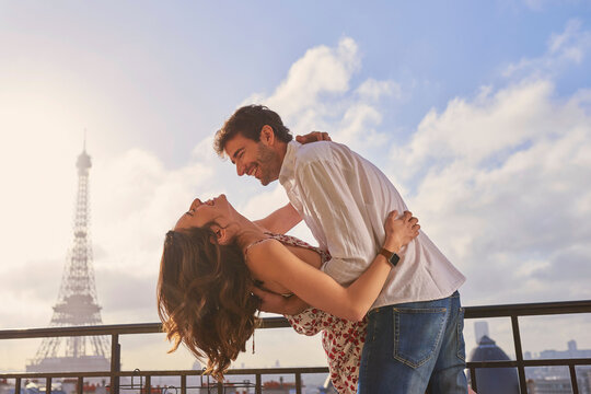 Love, Paris and couple together for a kiss, romantic time or balcony of apartment, hotel with Eiffel Tower in background. Partner, woman and man in France for vacation, travel or honeymoon holiday