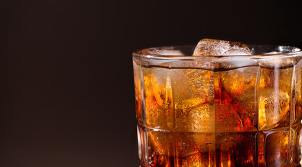 A glass of cola drink with ice cubes. Fresh cold sweet cola drink with ice on brown background with copy space.