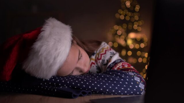 Child girl sleeping at the table near Christmas tree, she is waiting for Santa Claus, Christmas and holidays