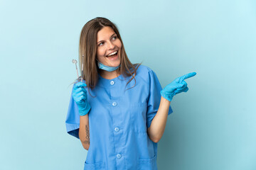 Slovak dentist holding tools isolated on blue background pointing finger to the side and presenting a product