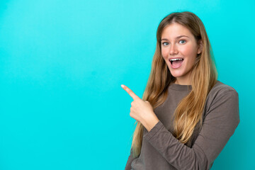 Young blonde woman isolated on blue background surprised and pointing side