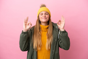 Young blonde woman wearing winter jacket isolated on pink background in zen pose