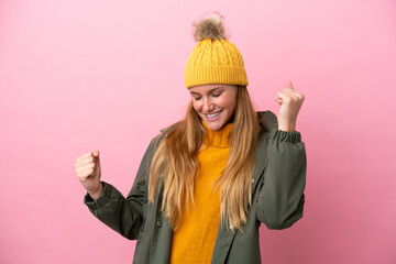 Young blonde woman wearing winter jacket isolated on pink background celebrating a victory